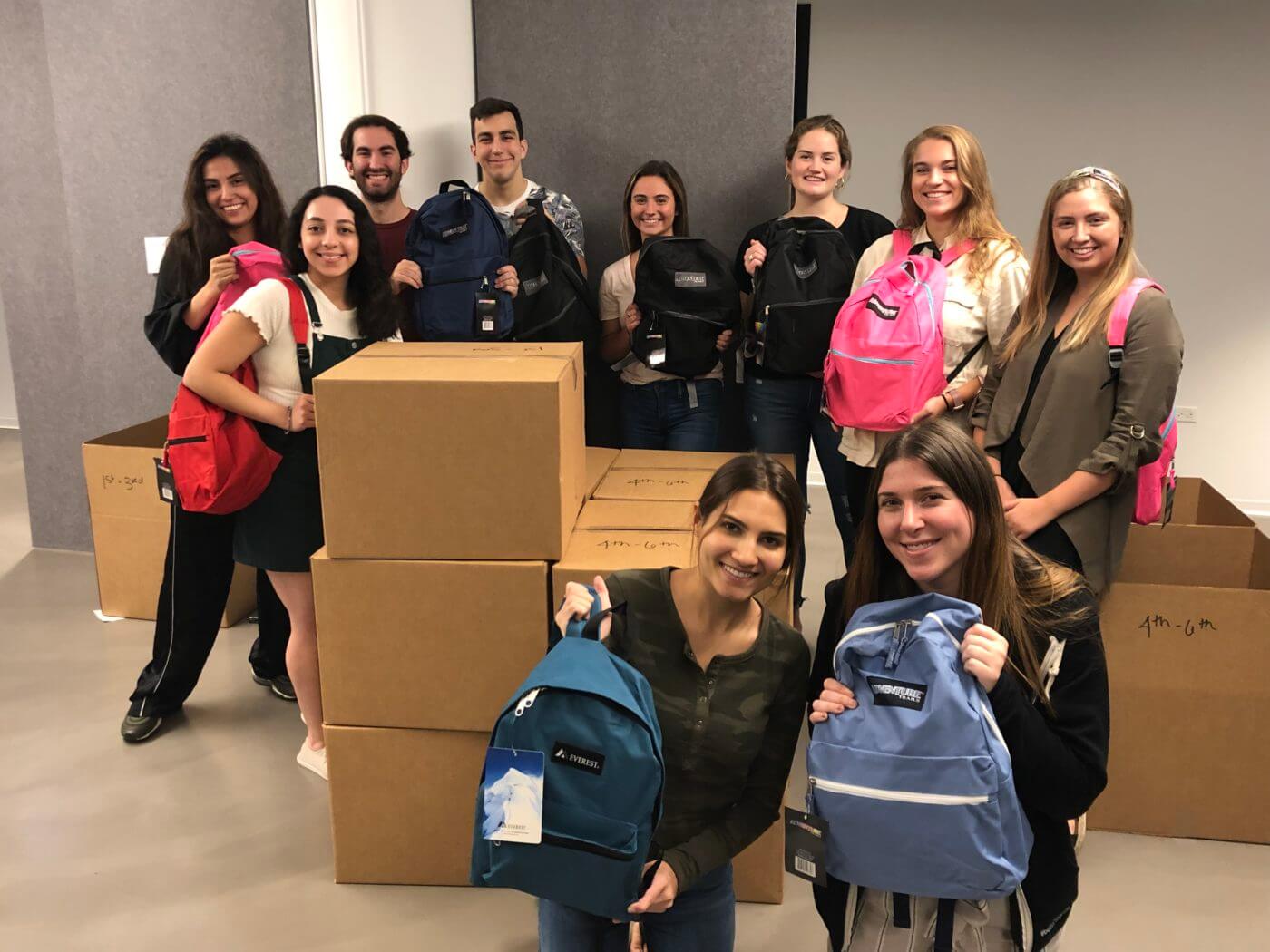men and women smiling with backpacks and cardboard boxes