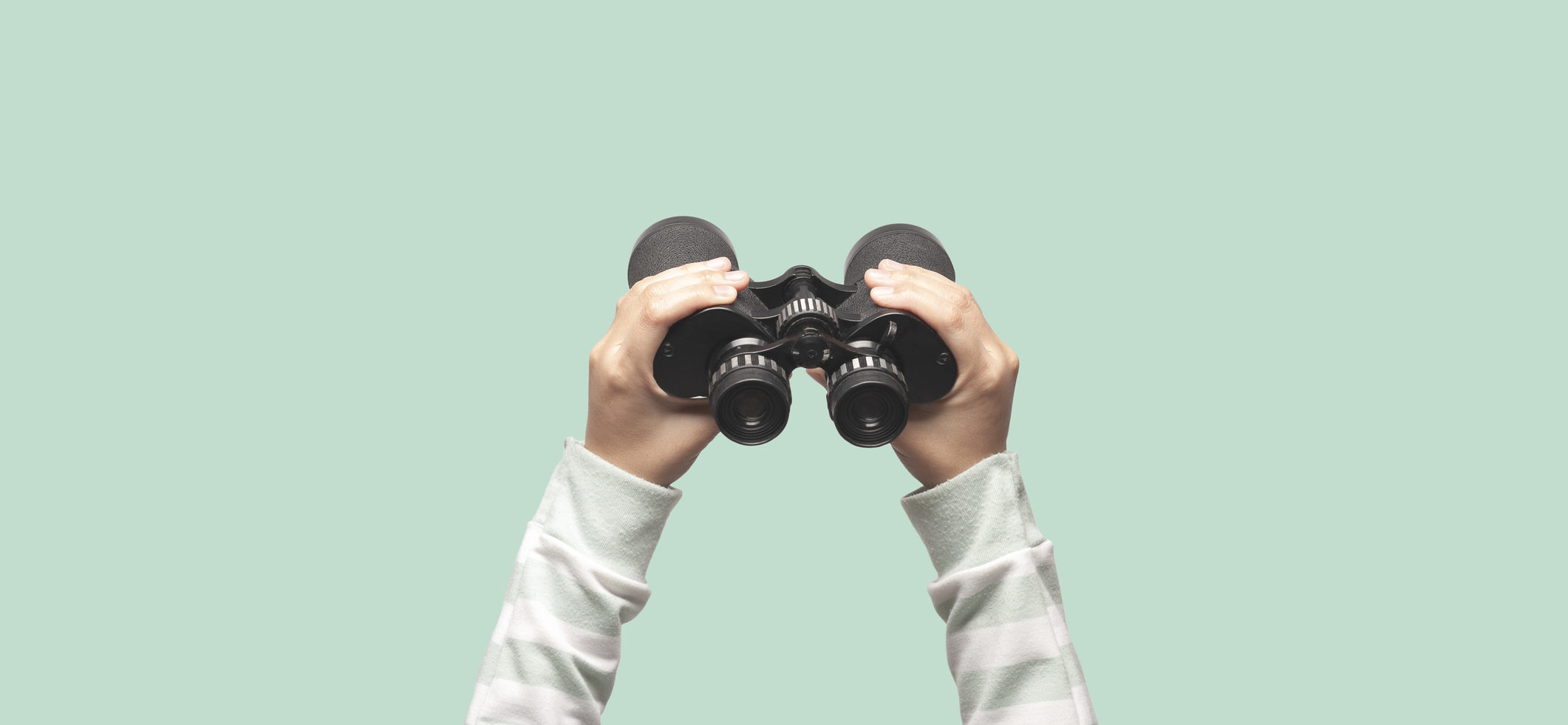 Pair of hands holding up a pair of binoculars against a green background