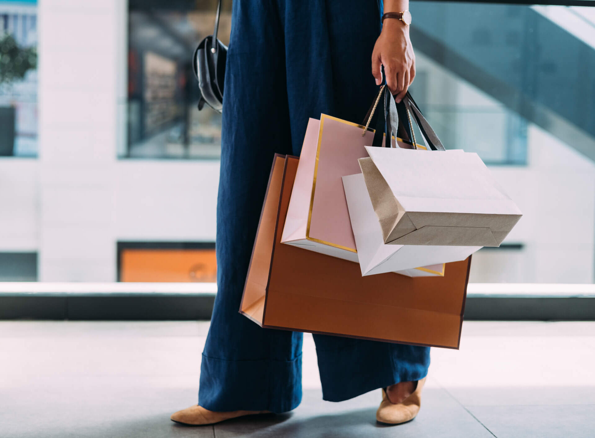 Image of a woman from the waist down wearing blue pants and carrying many shopping bags