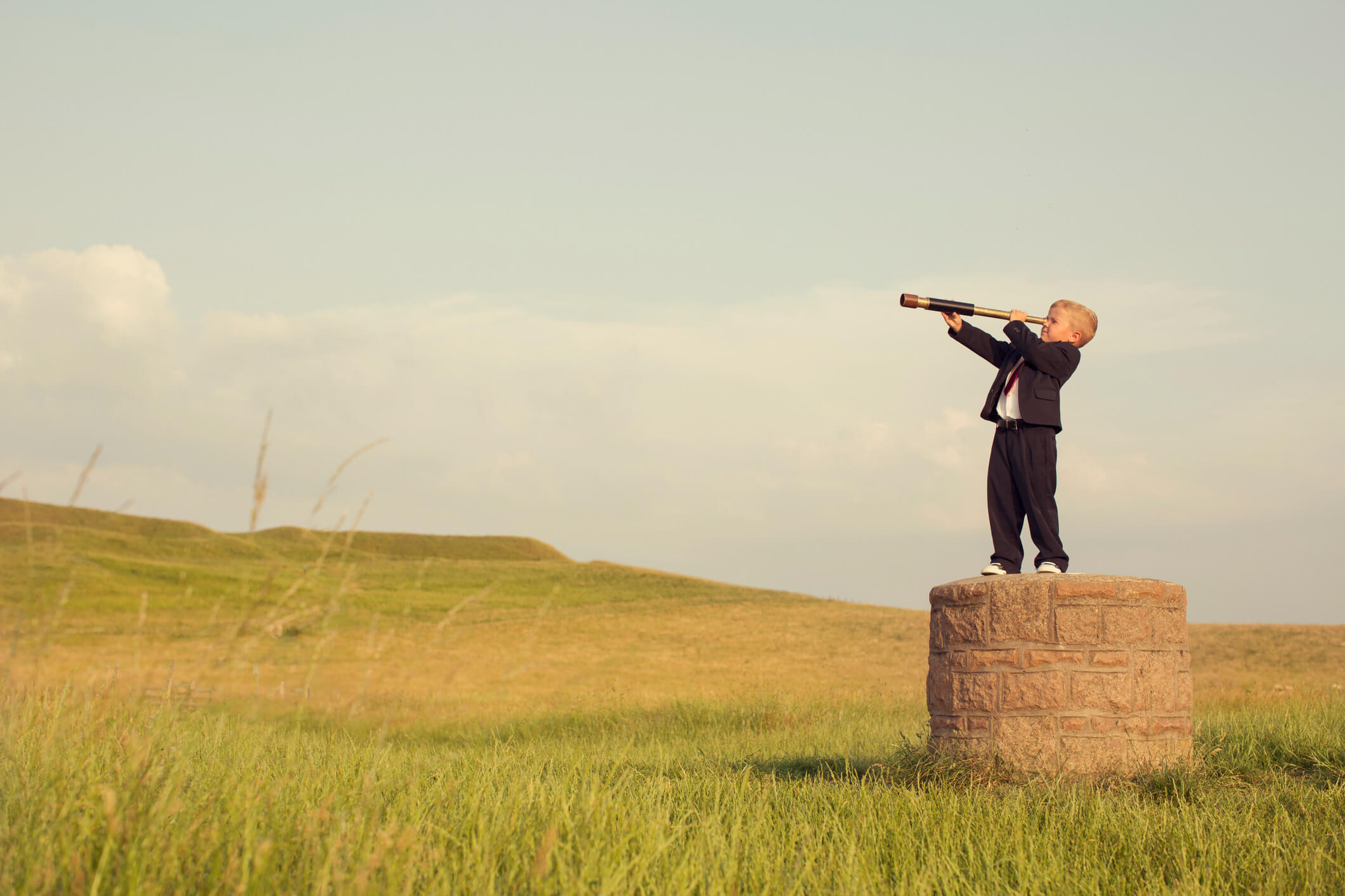 Little boy in business suit looking at a prairie through a telescope