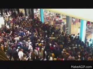 A large group of people rushing to get inside a retail store as soon as the gate opens, likely on Black Friday.