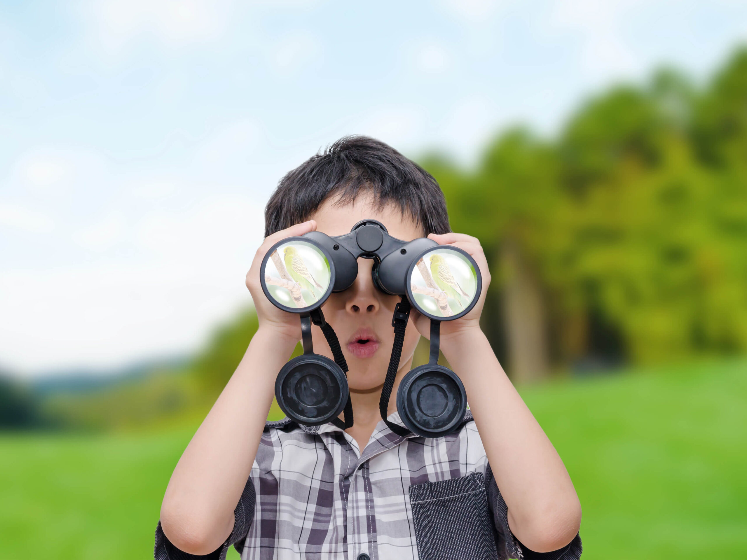 A child looking through binoculars with a surprised look on his face.