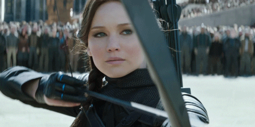 Actor Jennifer Lawrence playing Katniss Aberdeen in the movie "The Hunger Games," aiming at a target with her bow and arrow.