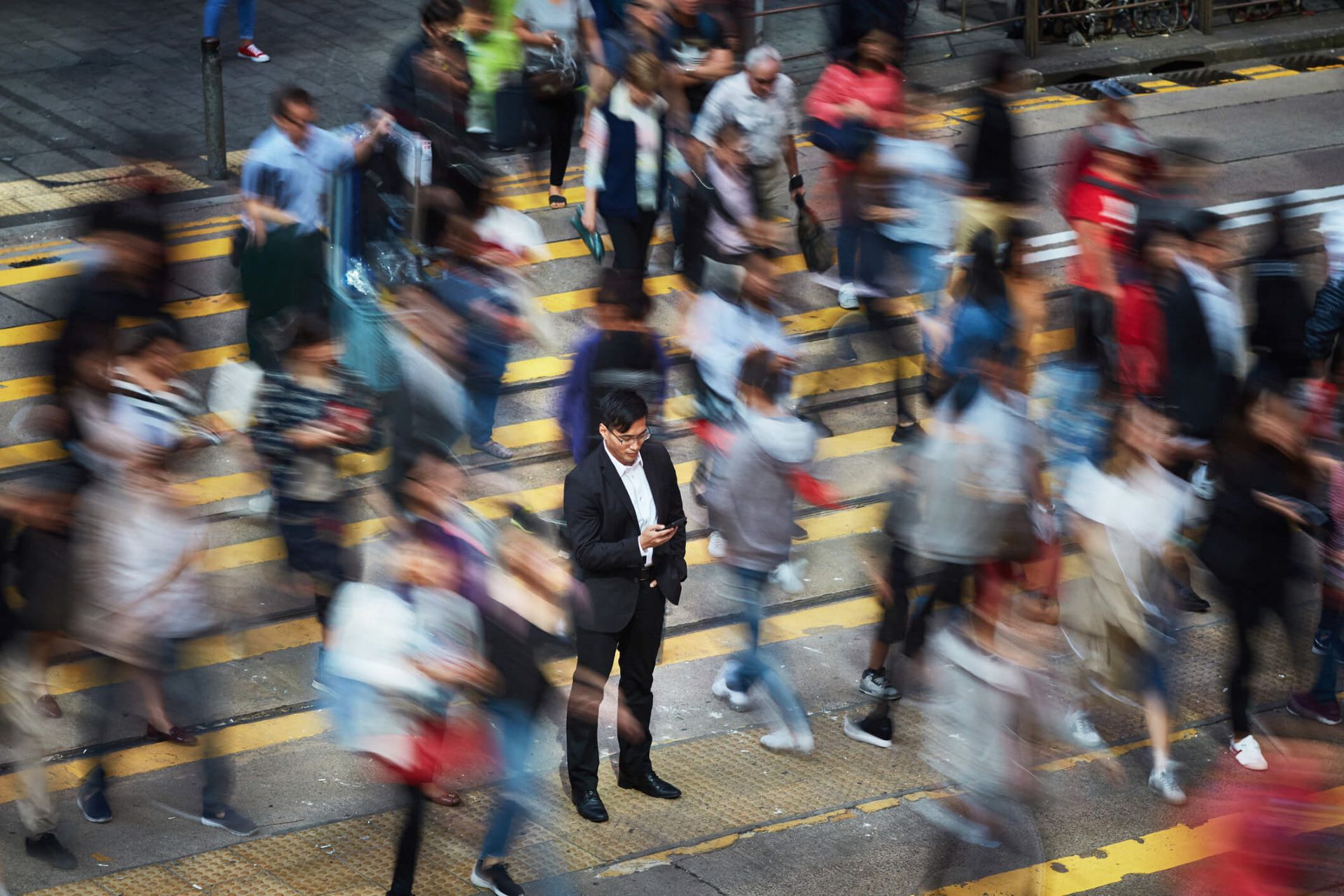 An image of a man in a blurry crowd. His attention has been captured by his cell phone.