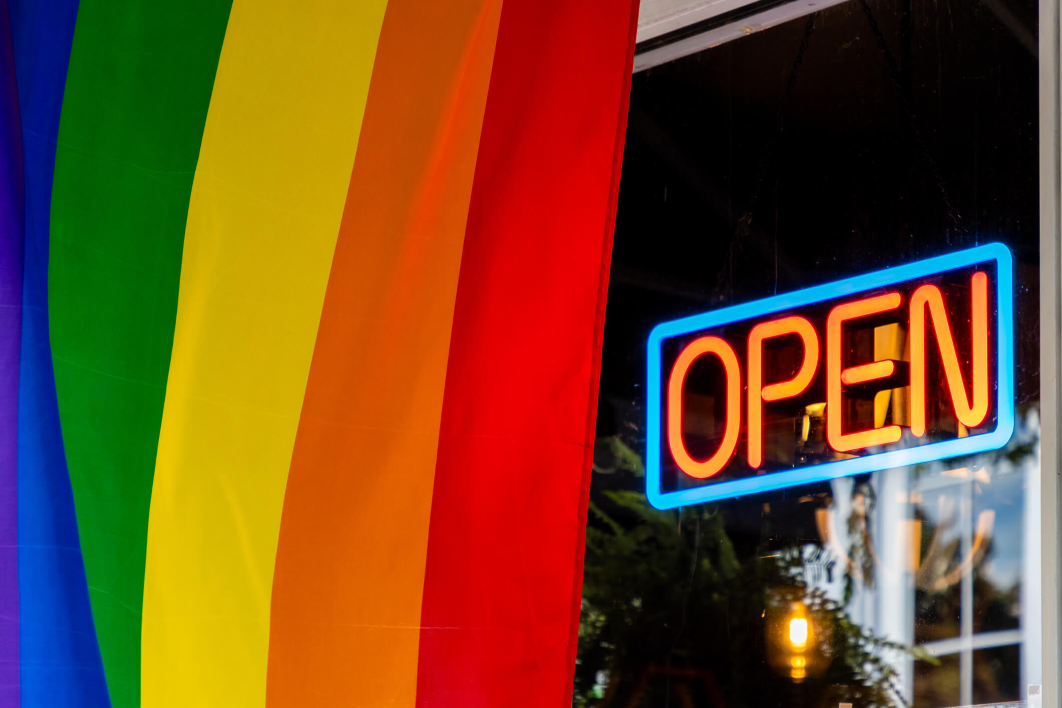 A rainbow pride flag flies in front of an open sign at a business