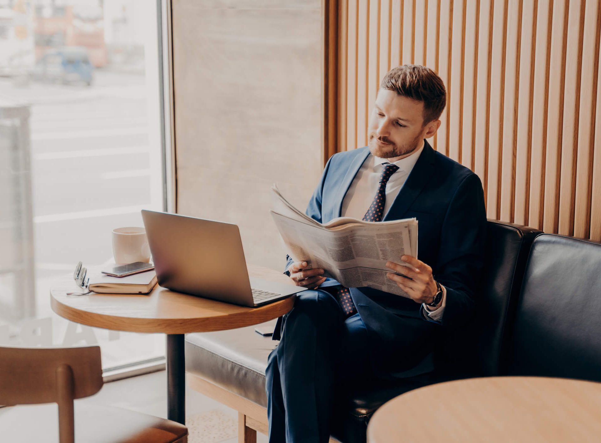 Businessman reading the newspaper with his laptop open