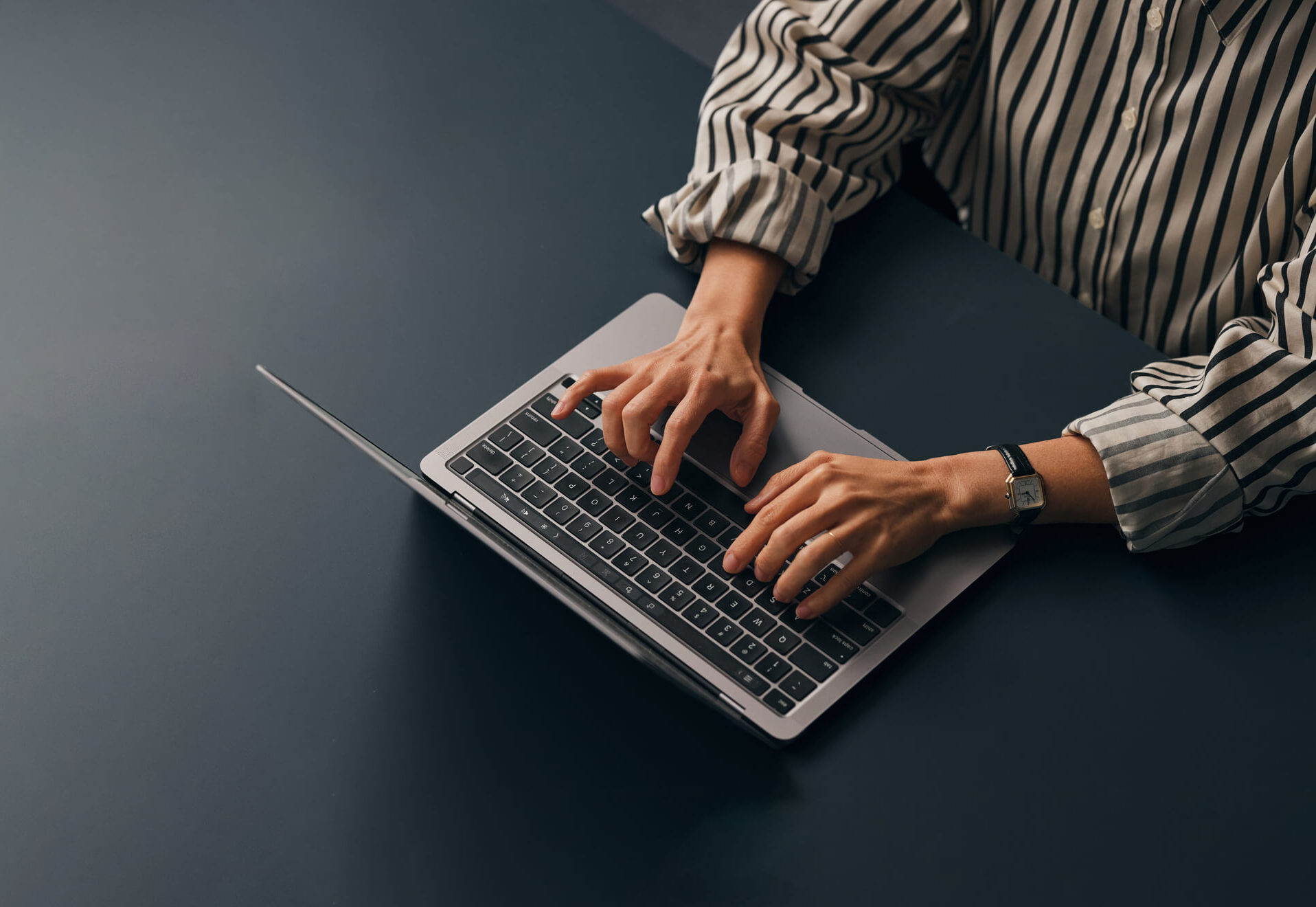 Person (only hands and arms are visible) wearing a striped shirt works at a computer