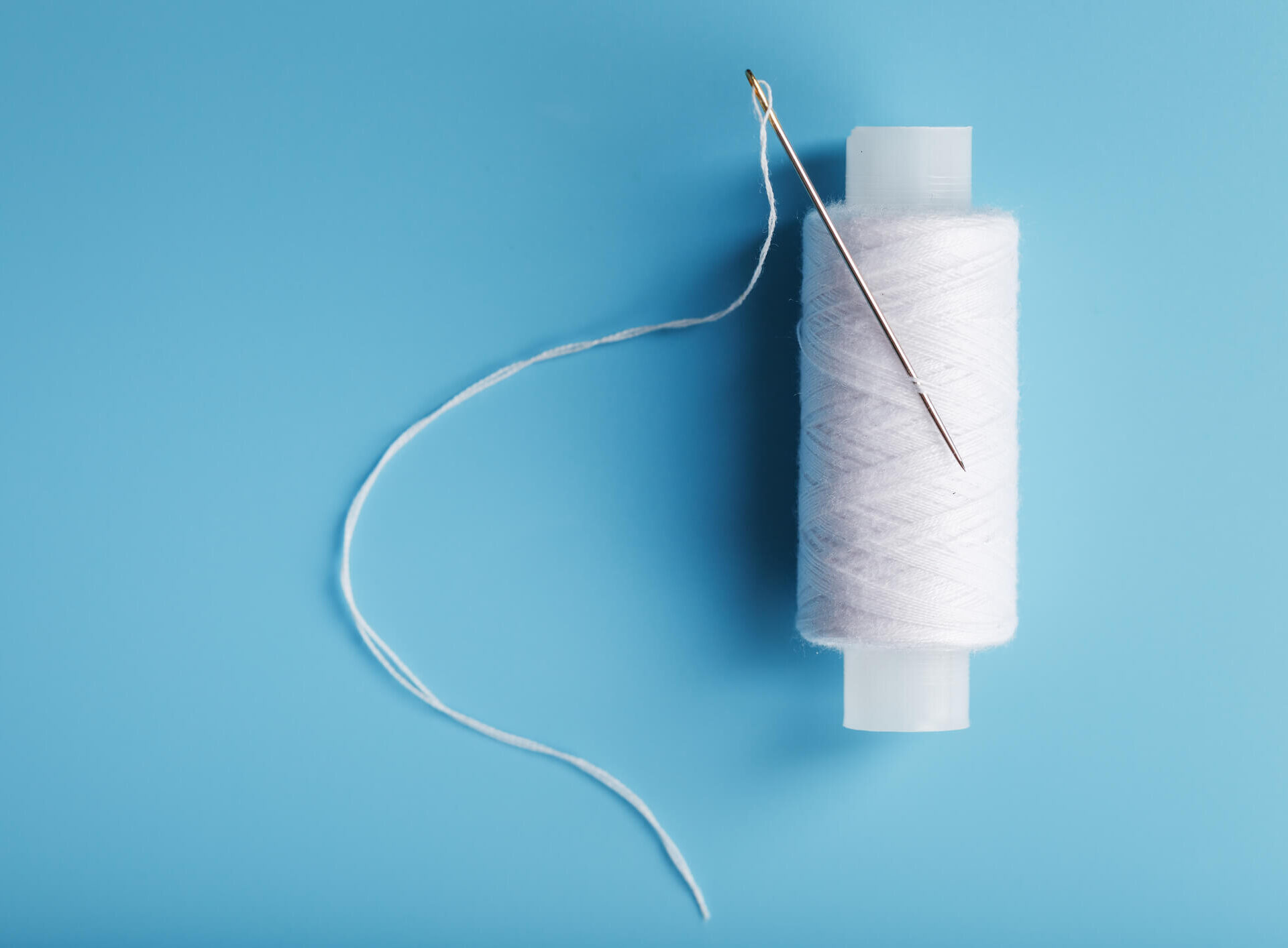 A skein of white thread with a needle on a blue background